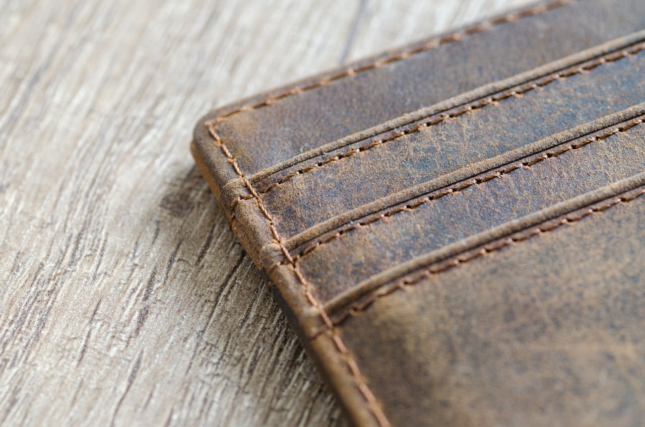 Detailed shot of a brown leather wallet on a textured wooden surface, showcasing stitching.